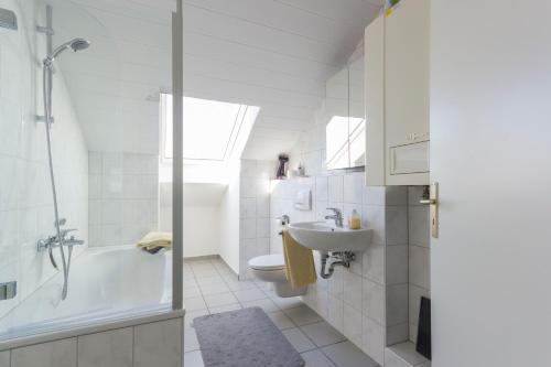 Baño blanco con bañera y lavamanos en favstay Industrialstyle 2-Zimmer 60qm mit Balkon, Panarbora Fernblick, 55" TV & Netflix, 55Mbit WLAN, Parkplatz, en Waldbröl