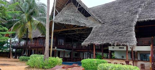 a building with a straw roof and a palm tree at Kena Beach Hotel in Matemwe