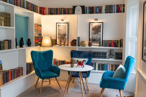a library with blue chairs and a table and bookshelves at Carlton Hotel in Ilfracombe