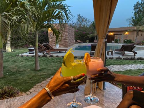 a person holding up two glasses with a drink at Hôtel La Belle Etoile & SPA in Saly Portudal