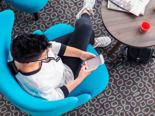a man sitting in a chair holding a cell phone at Mercure Blankenberge in Blankenberge