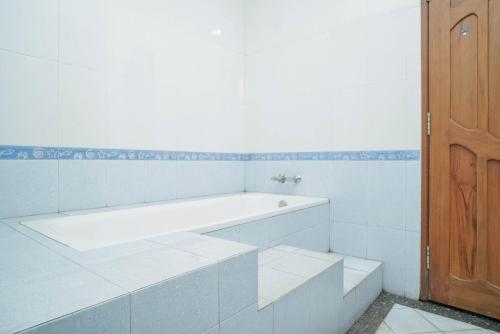 baño blanco con azulejos blancos y puerta de madera en KoolKost Syariah near Senayan City en Yakarta