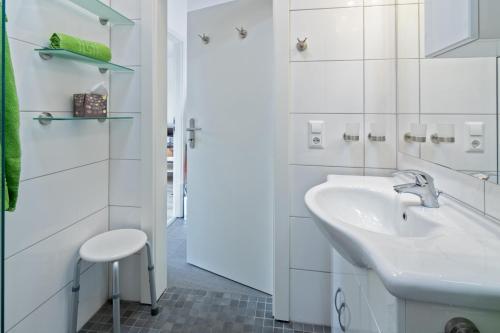 a white bathroom with a sink and a stool at Deichgraf in Dornumersiel