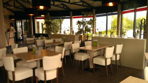 a restaurant with tables and white chairs and windows at Plaza Inn Berlin Süd Ludwigsfelde in Ludwigsfelde