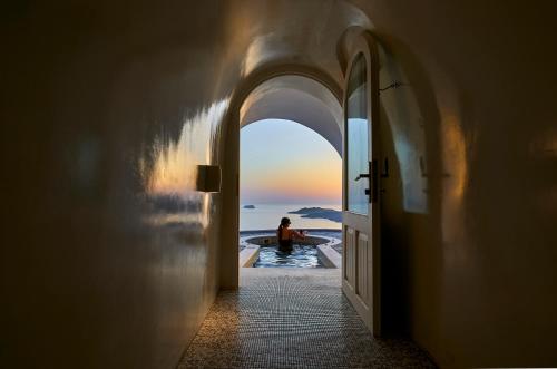 a man sitting in a swimming pool looking at the ocean at Petit Palace Suites in Fira