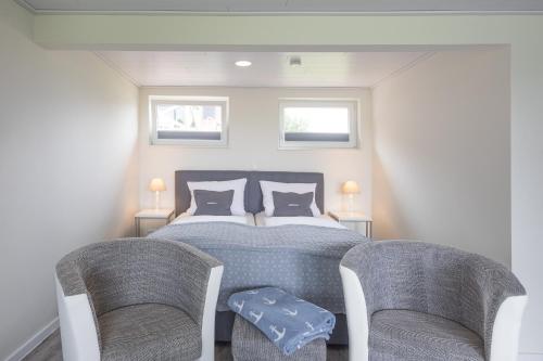 a bedroom with a bed and two chairs at Bungalow Neuwarft, Wohnung 2 in Dagebüll