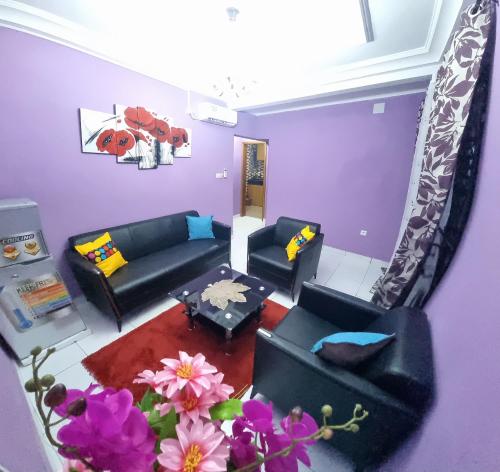 una sala de estar con paredes púrpuras, sofás y flores en Residence Sighaka - Gold Apartment - WiFi, Gardien, Parking en Douala