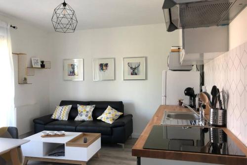 un salon avec un canapé noir et une cuisine dans l'établissement Cottage l'Echappée Belle, à Saint-Amand-les-Eaux