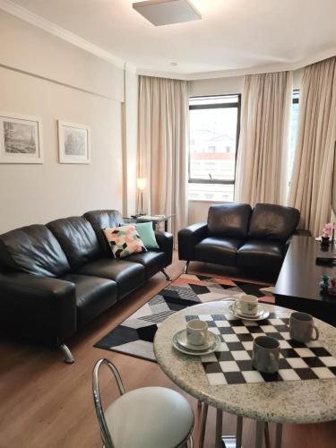 a living room with a black leather couch and a table at Flat Centro Campinas - L'Hirondelle 125 in Campinas