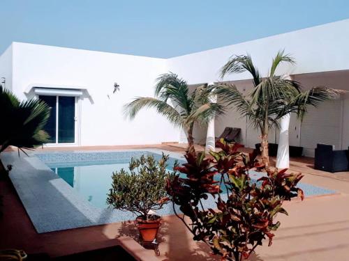 a house with a swimming pool and palm trees at Villa Charles Senghor in Saly Portudal