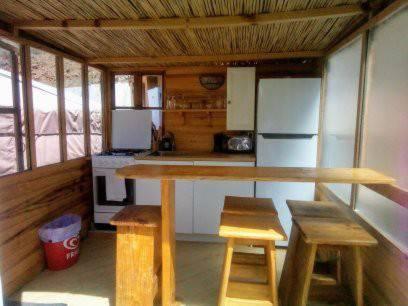 cocina con mesa, 2 taburetes y nevera en Eldorado Yurt, en Algarrobo