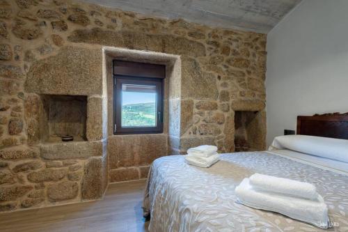 a stone walled bedroom with a bed and a window at O AGOCHO DA MOA in Mazaricos