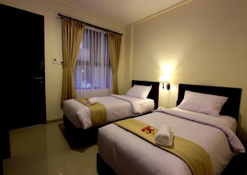 two beds in a hotel room with a window at Manggar Indonesia Hotel in Kuta
