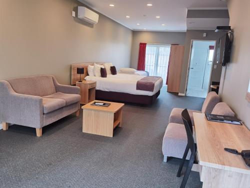 um quarto de hotel com uma cama, um sofá e cadeiras em Cornwall Motor Lodge em Palmerston North