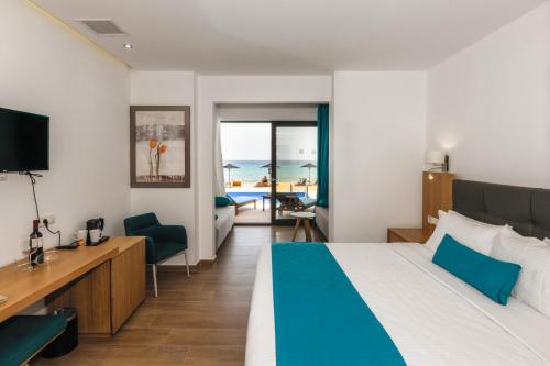 a bedroom with a bed and a desk with a television at Cavo Orient Beach Hotel & Suites in Tragaki