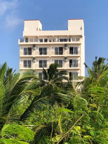 a tall white building with palm trees in front of it at iCom Marina Sea View in Maafushi