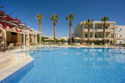 a large swimming pool with palm trees and a building at Mythos Suites Hotel in Tigaki