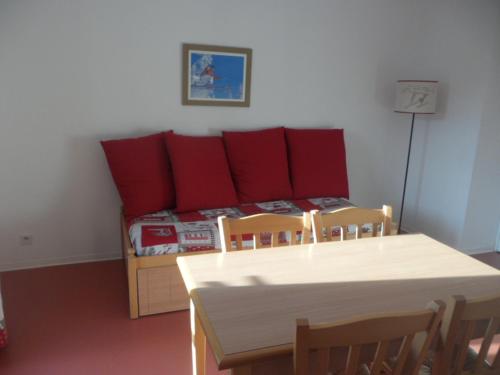 Cette chambre comprend une table et un lit avec des oreillers rouges. dans l'établissement LA JOUE DU LOUP T2 AU PIED DES PISTES, à La Joue du Loup