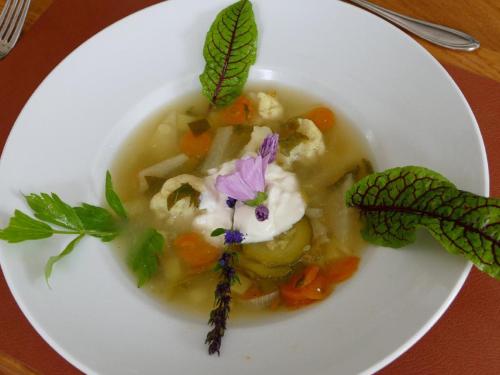 a white plate with a bowl of soup with vegetables at Kraftquelle Waldhäuser in Neuschönau