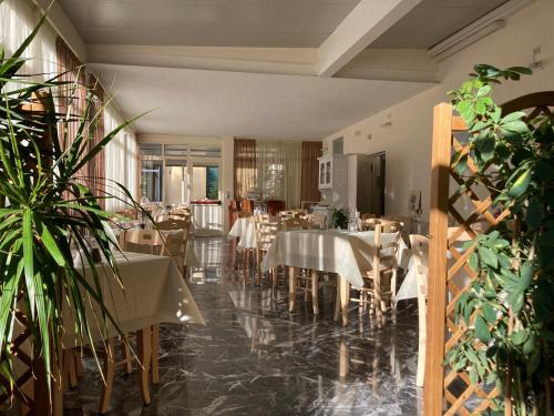 een restaurant met witte tafels, stoelen en planten bij Hotel Verdesolemare in Marina di Pietrasanta
