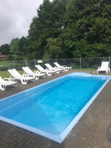 een zwembad met witte ligstoelen en een blauw zwembad bij Hotel Rezydencja Mazury SPA & Lake in Mrągowo