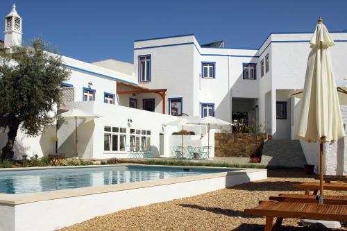 a white house with a swimming pool and an umbrella at A Casa da Cerca in Almodôvar