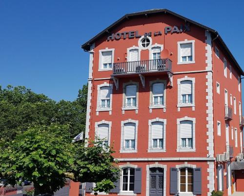 a red building with a balcony on the side of it at Hotel de La Paix in Oloron-Sainte-Marie