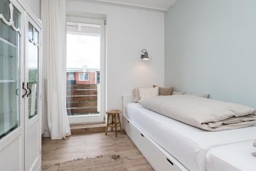 a white bedroom with a bed and a window at Nordlys - Local & Style in Westerland (Sylt)