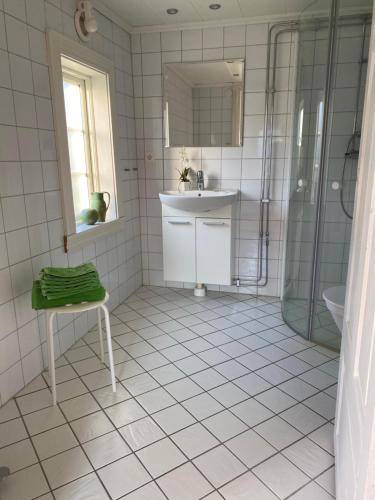 a white tiled bathroom with a sink and a shower at Lillstugan Lyckan in Kristdala