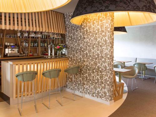 a restaurant with a bar with green stools at Mercure Bourg En Bresse in Bourg-en-Bresse
