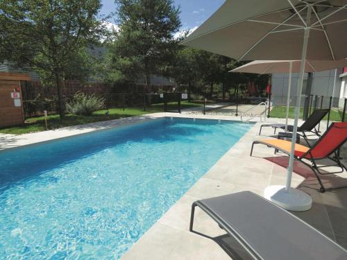 uma piscina com duas cadeiras e um guarda-sol em Ibis Saint-Genis-Pouilly Genève em Saint-Genis-Pouilly