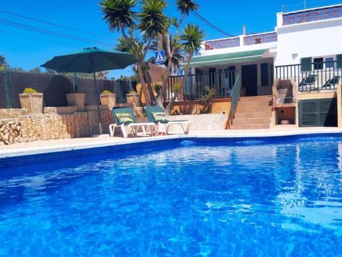 uma piscina com duas cadeiras e um guarda-sol ao lado de uma casa em Hermosa casa con piscina cerca de la playa de Punta Prima em Punta Prima