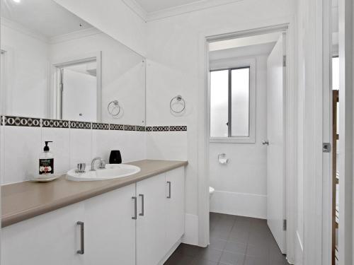 W białej łazience znajduje się umywalka i lustro. w obiekcie Beach Fun 11 Broadbeach Drive w mieście Carrickalinga