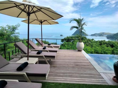 una terraza con sillas y sombrillas junto a una piscina en Paradise Garage Komodo Villa, en Labuan Bajo