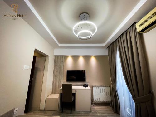 Habitación con escritorio, TV y lámpara de araña. en Hotel Holiday, en Podgorica