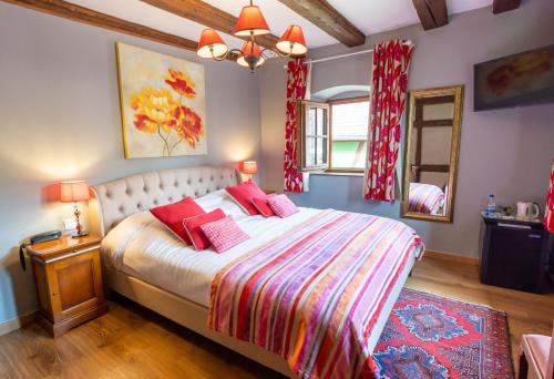 Un dormitorio con una cama con almohadas rojas y un espejo. en Hotel à l'Oriel, en Riquewihr