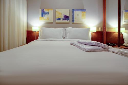 1 dormitorio con 1 cama blanca grande y 2 lámparas en Roomo Bela Cintra Residencial, en São Paulo