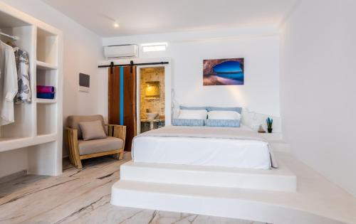 a white bedroom with a bed and a chair at The Colourful Land Milos in Klima