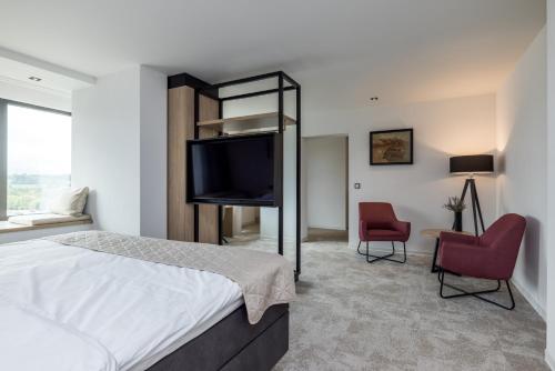 a bedroom with a bed and a tv and two chairs at Hotel de Rousch - 4 sterren Superieur in Heerlen