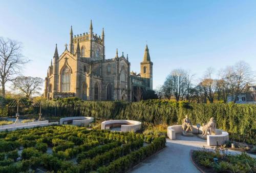 two people sitting on benches in a garden in front of a building at The Inn At Charlestown in Dunfermline