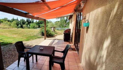 a table and chairs on a patio with an orange umbrella at Exclusive countryside retreat with private lake in Montrollet