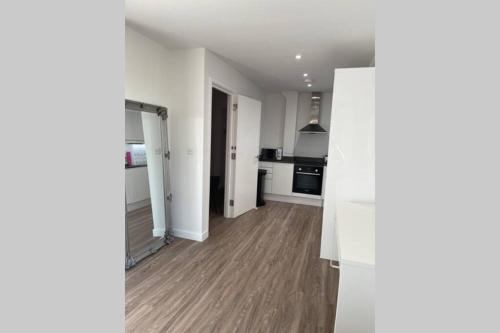an empty room with a kitchen with white walls and wooden floors at Croydon Gem Apartment - Fast train to the centre and free parking in Purley