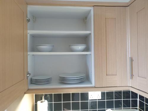 a kitchen cabinet with plates and bowls in it at London Luxury Apartments 5 min walk from Ilford Station, with FREE PARKING FREE WIFI in Ilford