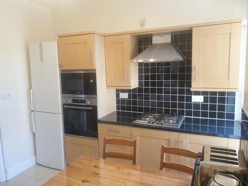 a kitchen with wooden cabinets and a blue tiled wall at London Luxury Apartments 5 min walk from Ilford Station, with FREE PARKING FREE WIFI in Ilford