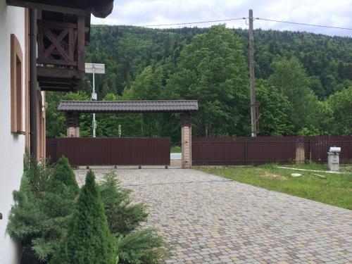 a stone walkway with a wooden fence and trees at Карпатський Готель Олександрія in Mykulychyn