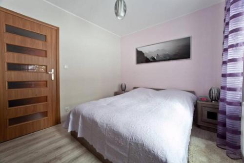 a bedroom with a white bed and a wooden door at Apartament Oliwkowy in Szklarska Poręba