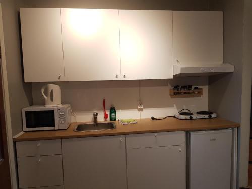 cocina con armarios blancos, fregadero y microondas en Skjólsteinar, en Grundarfjordur