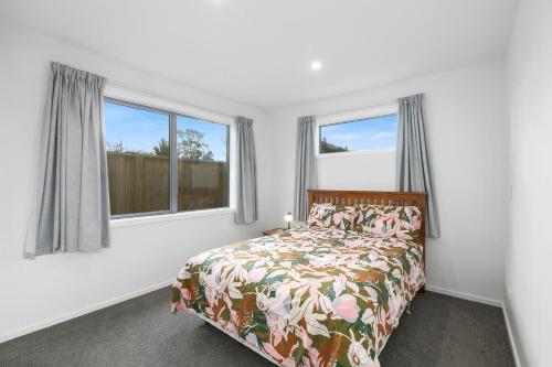 a bedroom with a bed and two windows at Karitane Beach Retreat - Karitane Holiday Home in Karitane