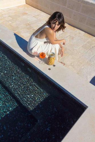 a woman in a white dress sitting next to a swimming pool at Borgo dei Lecci Puglia in Selva di Fasano