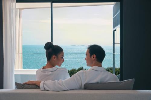 a man and woman sitting on a couch looking out a window at Bayphere Hotel Pattaya JC in Na Jomtien
